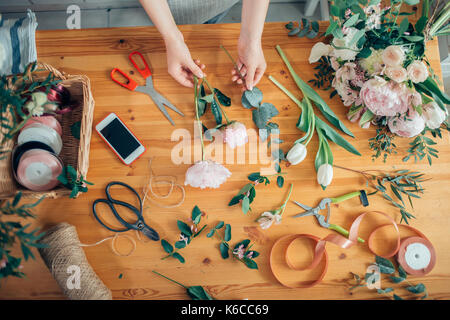 Mains d'un fleuriste contre desktop avec des outils de travail et rubans sur fond de bois Banque D'Images