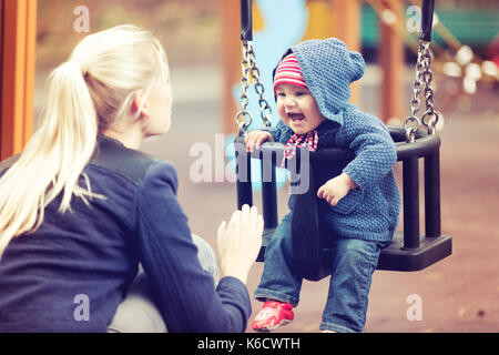 Mère avec son enfant s'amuser sur l'aire de swing sur jour d'automne Banque D'Images