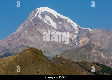 Jusqu'à la vue de la ville de Kazbegi en Géorgie, montrant l'église de trinité Gergeti Monastère et le sommet du mont Kazbek (Kazbeg) à 5047 mètres. Banque D'Images