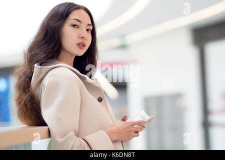 Belle jeune fille asiatique, utilise un téléphone mobile, l'arrière-plan, centre commercial ou centre d'affaires Banque D'Images