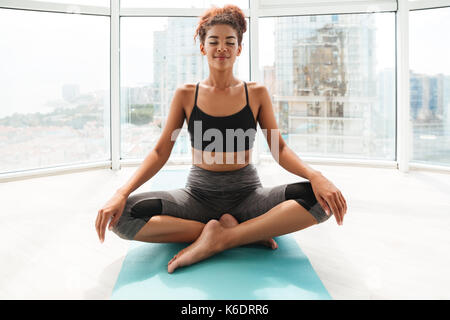 Long Shot de calme femme africaine faisant de l'exercice de yoga à la maison. Sitting on floor Banque D'Images