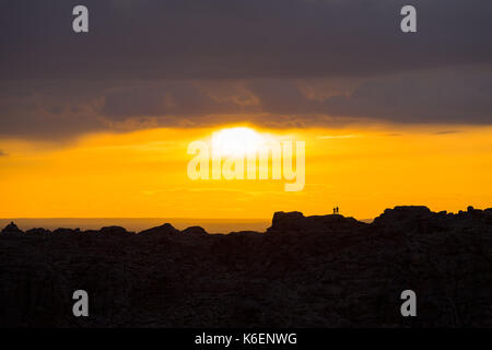 Silhouette de deux personnes debout sur la crête de lointain soleil nuages regarder breaking thru une orange ciel coloré au coucher du soleil en désert de Gobi en milieu rural mo Banque D'Images