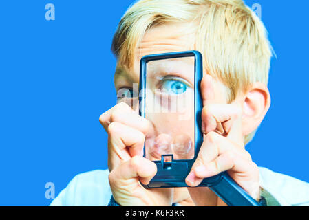 Portrait d'enfant jeune garçon blond à l'aide de loupe. concept de scientifique fou. isolé sur fond bleu l'entrée. Banque D'Images