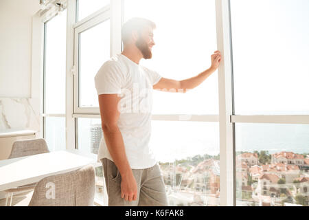 Vue latérale du beau barbu regardant la fenêtre à la maison Banque D'Images