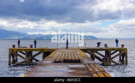 Cinq hommes de pêche à la fin de l'ancien quai à portencross, North Ayrshire, Ecosse un jour nuageux avec l'île d'arran à l'horizon Banque D'Images