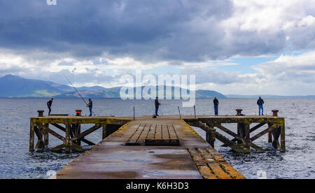 Cinq hommes de pêche à la fin de l'ancien quai à portencross, North Ayrshire, Ecosse un jour nuageux avec l'île d'arran à l'horizon Banque D'Images