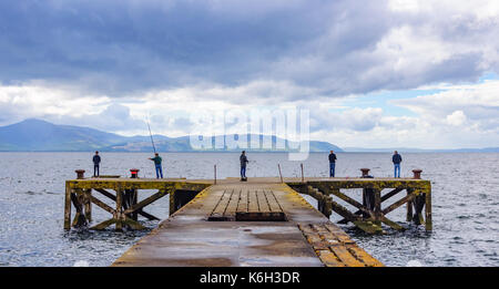 Cinq hommes de pêche à la fin de l'ancien quai à portencross, North Ayrshire, Ecosse un jour nuageux avec l'île d'arran à l'horizon Banque D'Images