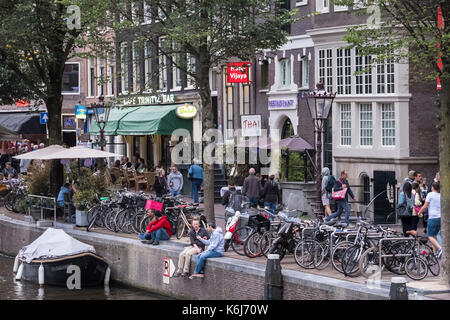 Rue animée le long d'un canal dans le centre d'Amsterdam, avec ses bars et restaurants et les personnes bénéficiant de la ville. Banque D'Images