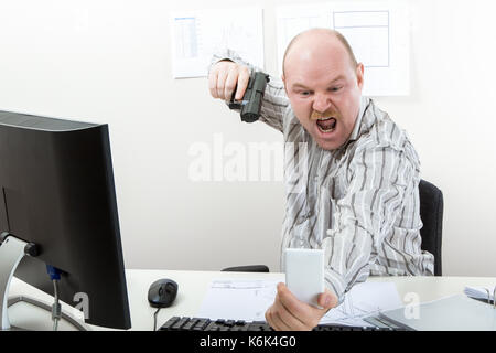 Businessman visant gun on mobile phone at desk Banque D'Images