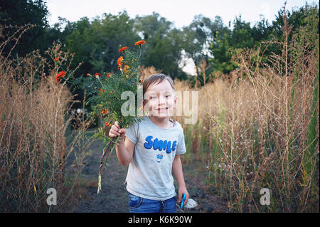 Portrait of smiling boy joyeux et dans la nature avec bouquet de fleurs sauvages. il regarde la caméra. dans un t-shirt avec une inscription smile Banque D'Images