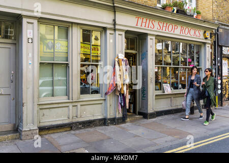 Deux femme marche passé Cette boutique Rocks secondhand des vêtements, des meubles et de livres à Brick Lane, London Banque D'Images