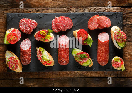 Variété de mini-sandwiches et bruschettes avec fromage à la crème, légumes et saucisson. sandwiches avec du fromage, de concombre, de radis, de tomates, de salami, de thym Banque D'Images