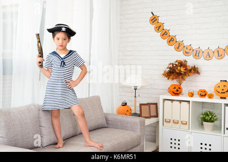 La confiance grave capitaine naughty girl holding un pistolet jouet pirate s'amuser pour halloween de l'article sur canapé à la maison Banque D'Images