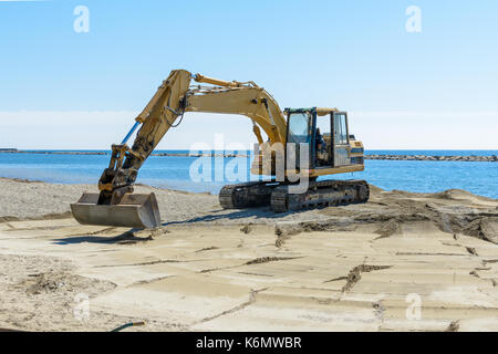 Que l'excavateur travaille sur la plage pour lisser le sable avant le début de la saison d'été Banque D'Images
