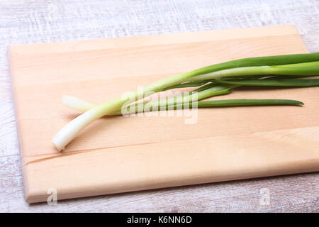 Petit paquet d'oignons verts frais lavés avec de longues tiges et racines minuscules sur la table en bois. Banque D'Images