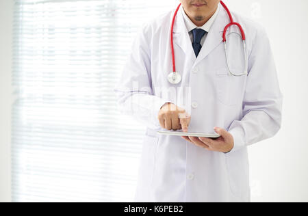 Doctor posing inconnu à l'aide de tableau numérique avec arrière-plan lumineux, il porte un stéthoscope numérique . table dans le bureau, il est vêtu d'un stethosco Banque D'Images