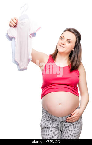 Young happy future mère choisit des vêtements pour l'enfant sur un fond blanc Banque D'Images