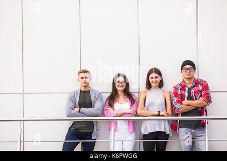 Groupe de quatre jeunes gens souriants portant des vêtements élégants à la caméra au comité permanent à la lumière. Banque D'Images