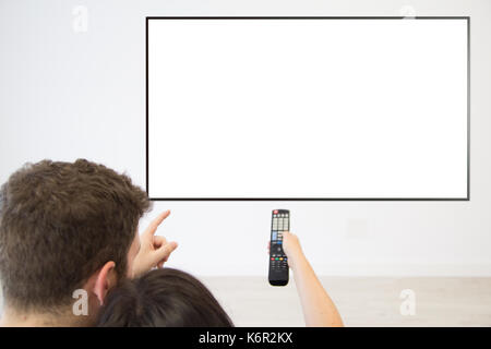 Vue arrière couple regardant la télévision à la maison. écran blanc. Banque D'Images