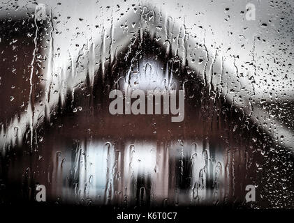 Voir une maison privée en temps de pluie par la fenêtre humide. Banque D'Images