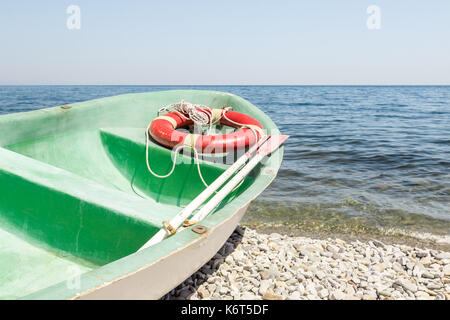 Ancien canot de pagaie verte sur une plage de galets. Il y a des pagaies et bouée rouge avec une corde à l'intérieur le bateau de patrouille. Banque D'Images