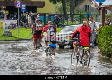 Sarbinowo, Pologne - août 2017 : trois hommes à vélo dans une eau profonde sur une route inondée après une pluie torrentielle Banque D'Images