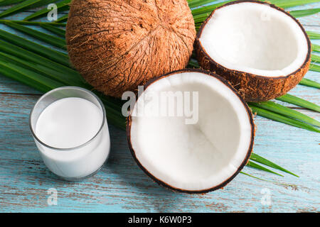 Les moitiés de noix de coco vert feuille et le lait de coco en verre sur fond sombre. Vue de dessus avec copyspace Banque D'Images