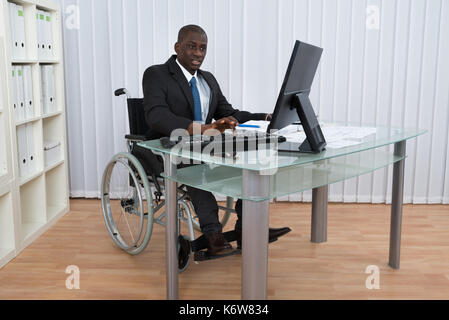 Portrait of happy young woman working in office assis sur fauteuil roulant Banque D'Images