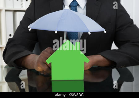 Close-up of businessman mains protéger chambre modèle avec parapluie à 24 Banque D'Images