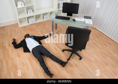 Jeune inconscient african businessman lying on floor in office Banque D'Images