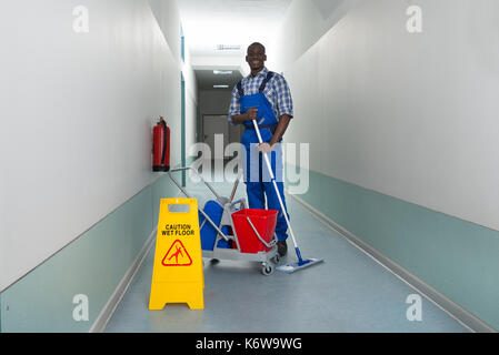 Les jeunes professionnels janitor holding mop avec godet et signe sol humide dans le couloir Banque D'Images