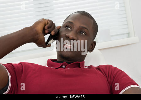 Portrait of young African man sitting on couch talking on cellphone Banque D'Images