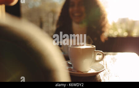 Gros plan de la vapeur chaude tasse de café sur une table avec vue brouillée de deux femmes parlant. Femme parlant à son ami assis à une table de café. Banque D'Images