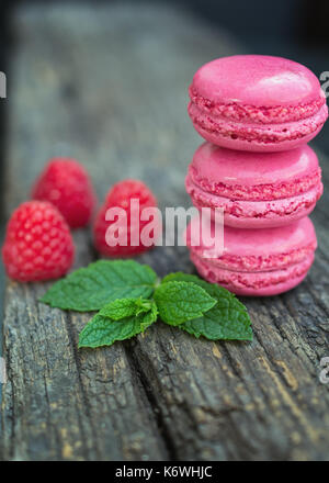 Délicieux macarons à la framboise avec des framboises fraîches et une feuille de menthe présenté sur un plateau en bois Banque D'Images