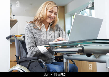 Mobilité woman in wheelchair using laptop at home Banque D'Images