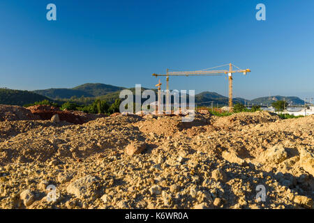 Rez-de-chaussée du nouveau bâtiment chantier près de la montagne avec de nombreuses grues jaunes sur fond de ciel bleu. Banque D'Images