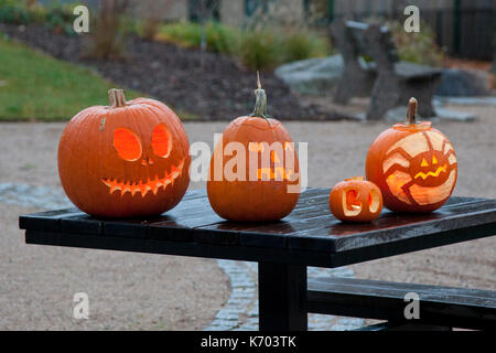 Quatre jack-o-lanternes ou citrouilles sculptées avec des visages effrayants allumé s'asseoir sur une table. Banque D'Images