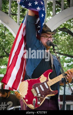Un homme de race blanche singer soulève un drapeau américain au cours d'un festival de musique local extérieur. Banque D'Images