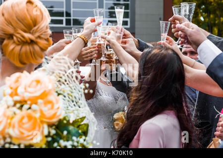 Les invités au mariage de trinquer les verres de champagne avec les jeunes mariés dans l'arrière-plan. Banque D'Images