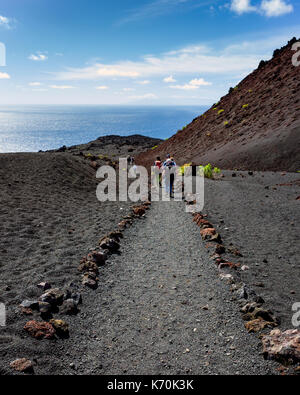 Los Volcanes de Teneguía, Fuencaliente, La Palma. Une vue sur le paysage aride autour du volcan. Très peu de végétation est en mesure de se développer dans ce milieu difficile ce qui en fait un paysage très clairsemée.Les randonneurs à pied le long du sentier sur une visite guidée, la mer peut être vu dans l'avant-plan. C'est une journée ensoleillée avec quelques nuages en mouvement rapide contraste avec le ciel bleu. Banque D'Images