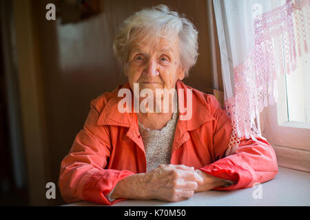 Femme âgée en veste rouge sitting at table portrait. Banque D'Images