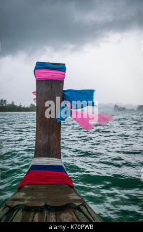 L'avant d'un bateau à longue queue avec la prière des écharpes à vers la terre ferme dans la distance et les écharpes au vent, mer d'Andaman, Krabi, Thaïlande Banque D'Images