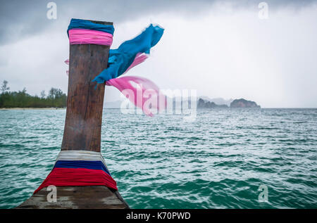 L'avant d'un bateau à longue queue avec la prière des écharpes à vers la terre ferme dans la distance et les écharpes au vent, mer d'Andaman, Krabi, Thaïlande Banque D'Images