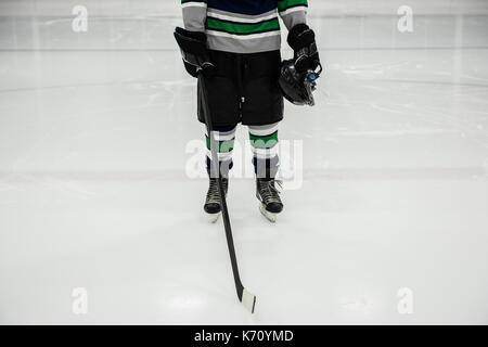 La section basse de l'homme joueur tenant le bâton de hockey sur glace et casque en rink Banque D'Images