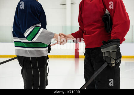 Section intermédiaire de joueurs de hockey masculin avec des bâtons shaking hands at rink Banque D'Images