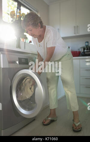 Senior woman enfiler ses vêtements en machine à laver à la maison Banque D'Images