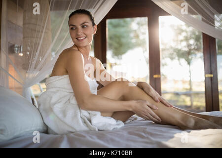 Woman applying lotion, assis sur un lit à baldaquin en chalet Banque D'Images