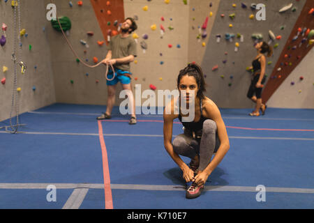 Portrait de femme lacet attachant bien que les athlètes d'un mur d'escalade en salle de sport à l'arrière-plan Banque D'Images