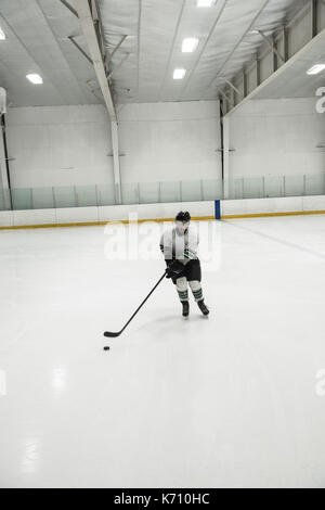 Toute la longueur de l'homme joueur pratiquant le hockey sur glace à la patinoire éclairée Banque D'Images