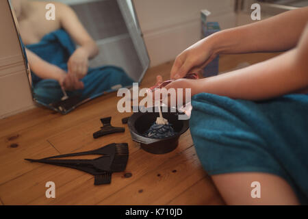 Mid section of woman mixing hair dye dans un bol avec la réflexion sur le miroir de salle de bains Banque D'Images